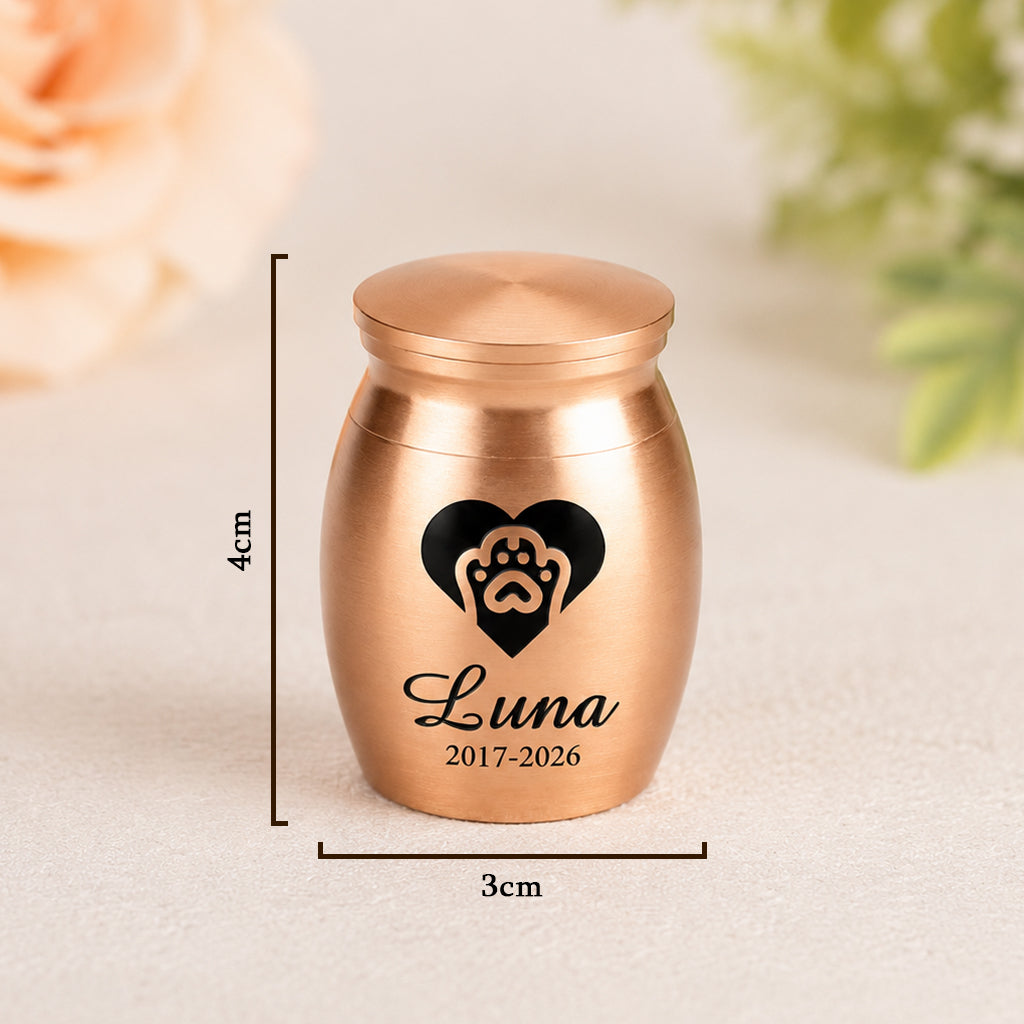 Small pet memorial keepsake urn with engraved paw print displayed on a soft surface