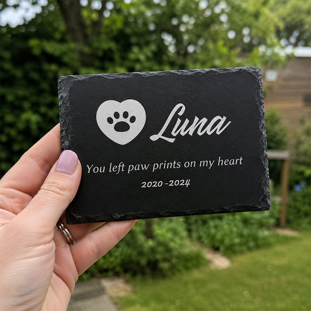 Engraved slate memorial plaque leaning against a stone wall in an outdoor garden setting