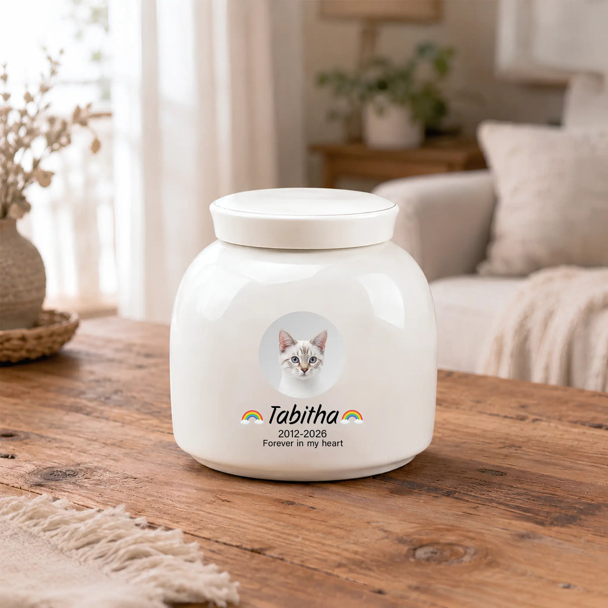 Cream ceramic rainbow cat urn on a wooden coffee table, showing the printed photo, name and "Forever in my heart"