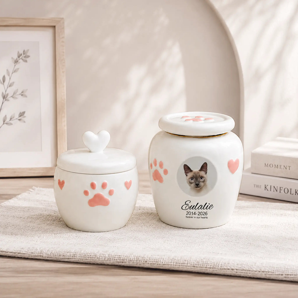 Pink paw print cat urn set displayed on a shelf, the larger jar showing a photo window with the cat's name and years