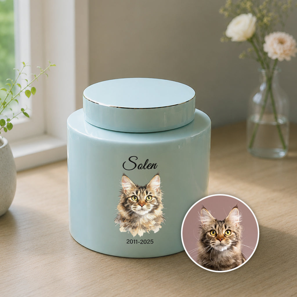 Close-up of watercolor cat portrait and engraved dates on a teal ceramic cremation urn