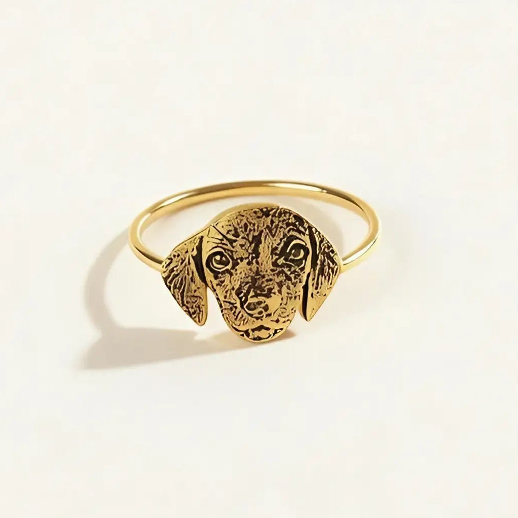 A gold-colored adjustable ring featuring a detailed, textured dog head charm, photographed on a clean, solid off-white background.