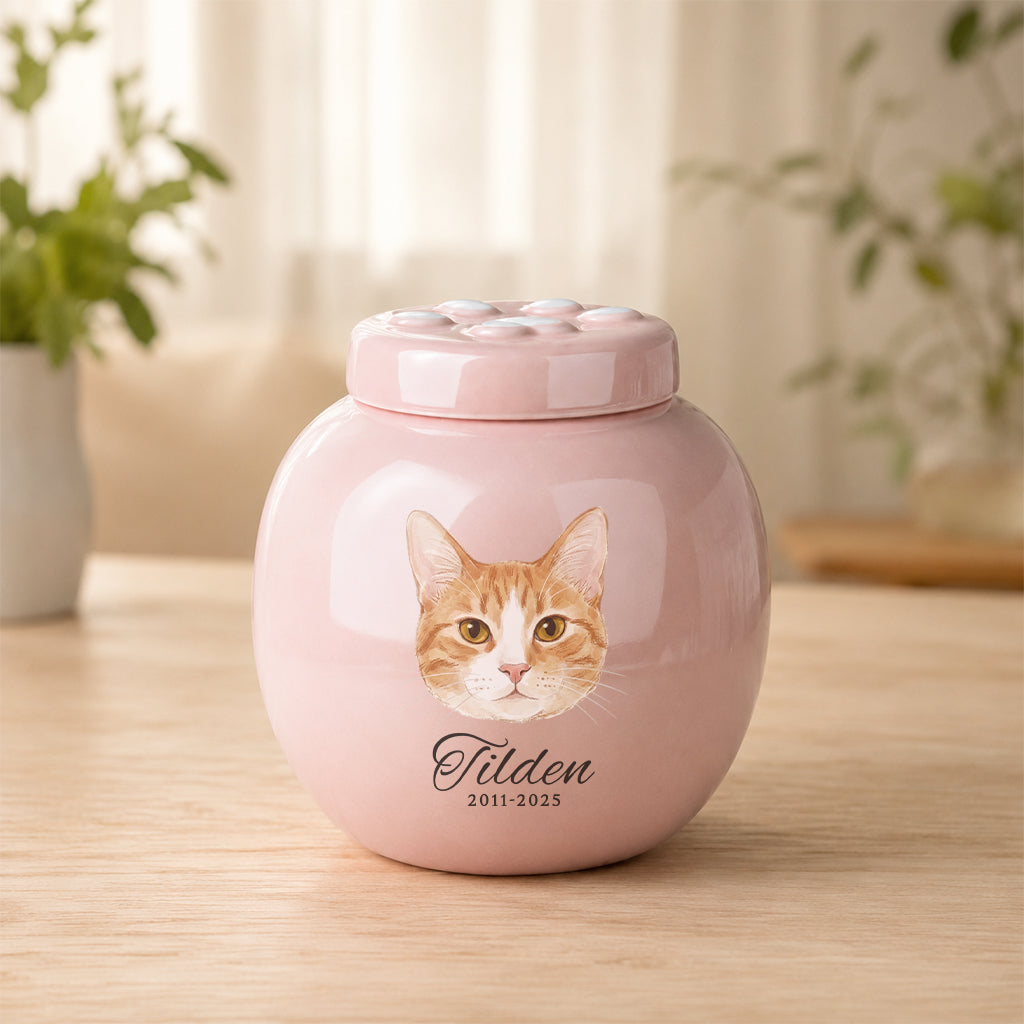 Soft pink ceramic cat cremation urn with paw print lid and personalized cat portrait on the front