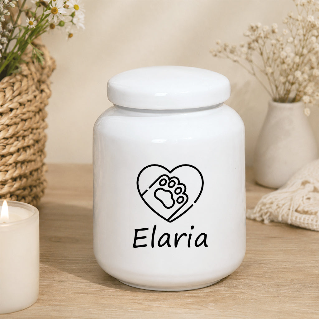 Ceramic pet cremation urn with engraved name displayed on a wooden surface in a home setting
