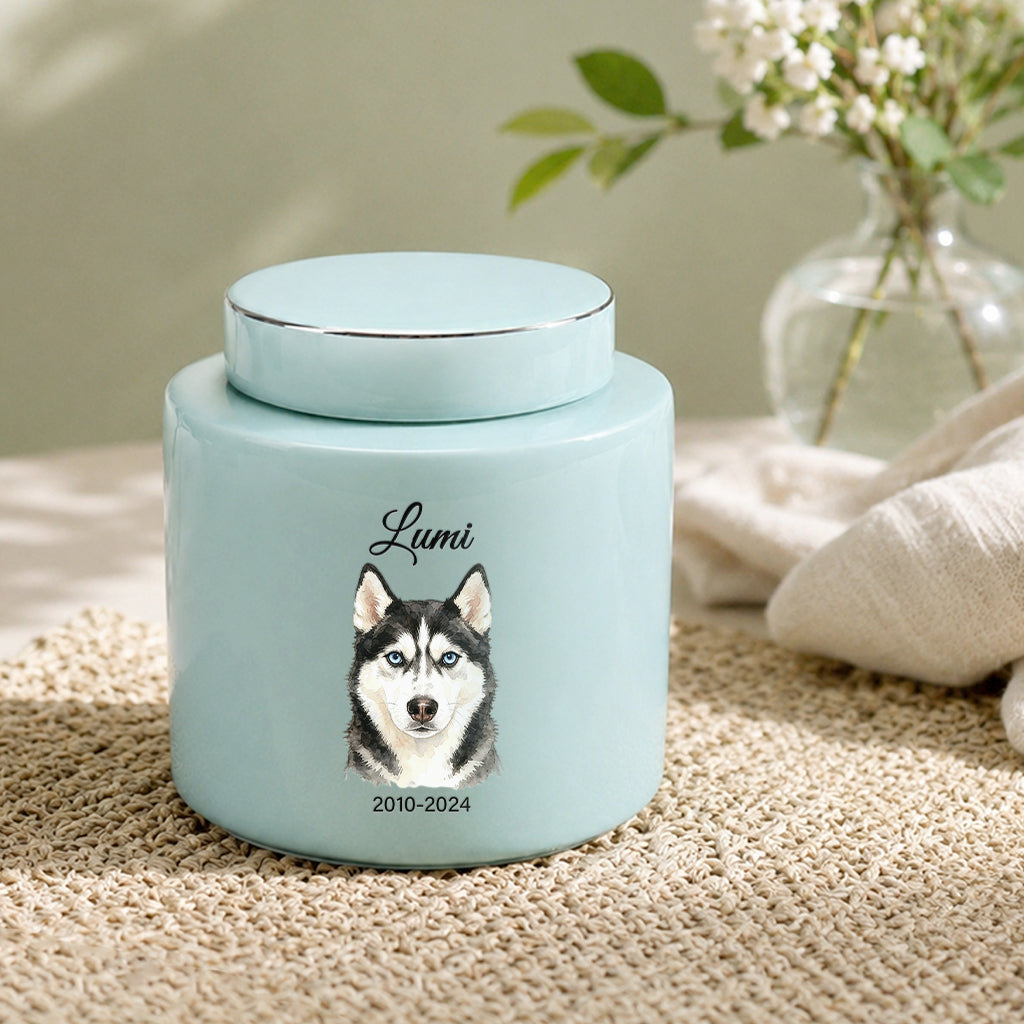 Close-up of watercolor dog portrait and engraved dates on a teal ceramic cremation urn