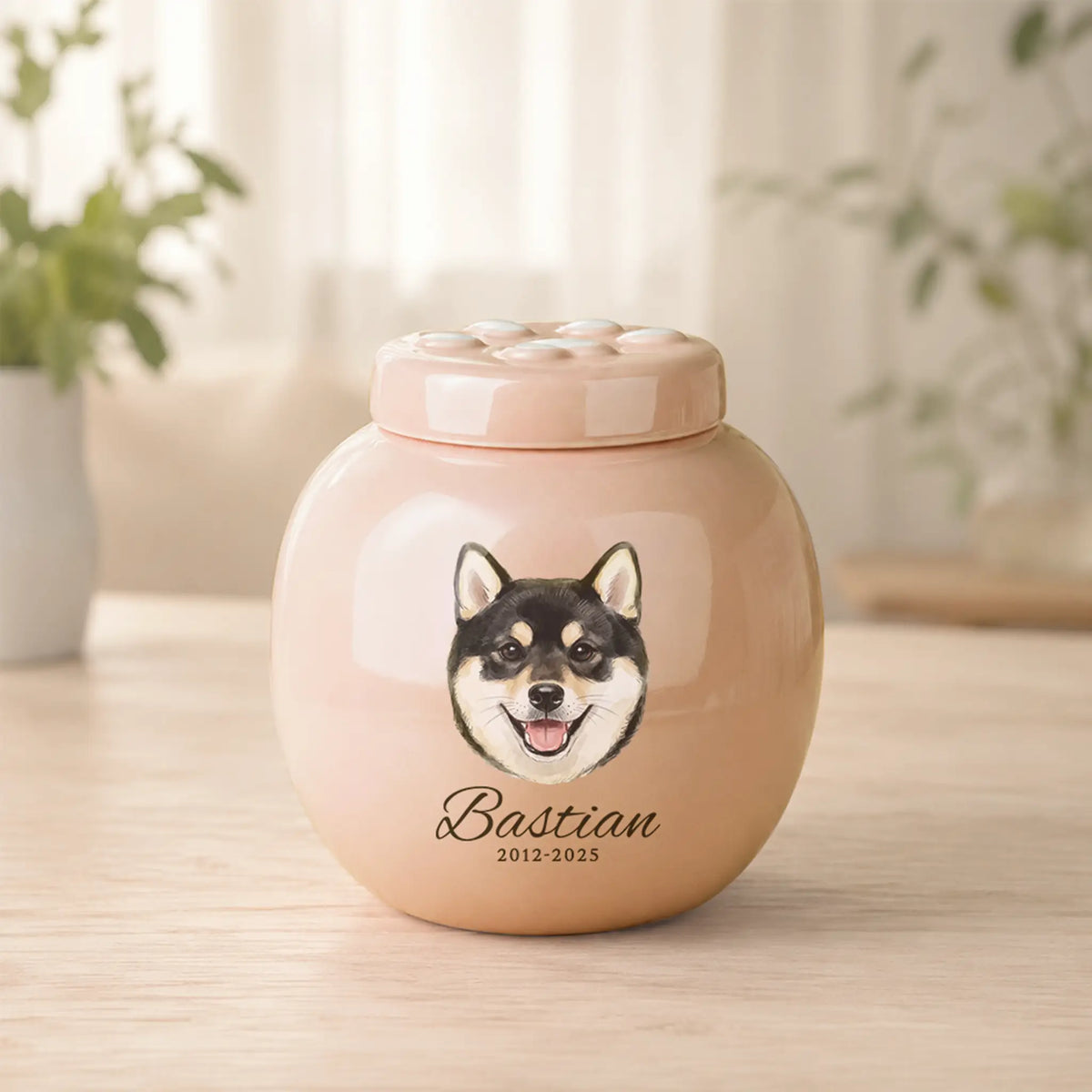 Personalized pink ceramic dog cremation urn with a hand‑painted watercolor pet portrait, the name Bastian, memorial years 2012–2025, and a paw‑print lid, displayed on a wooden table.